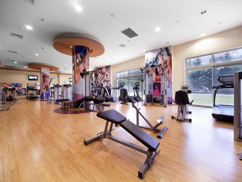 Bright gym with wooden floor, various exercise machines, and large windows.