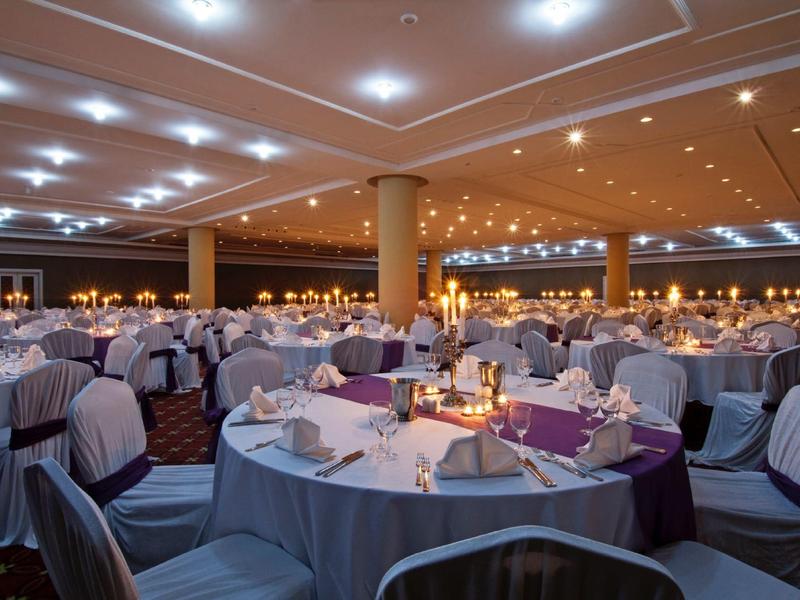 Large elegantly decorated banquet hall with round tables and covered chairs.