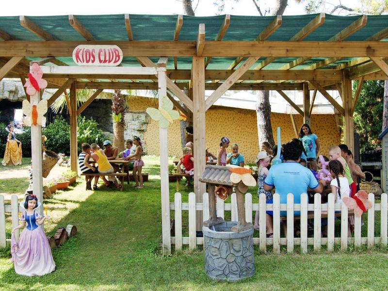 Children play and sit under a wooden pergola in a garden with wooden fences.