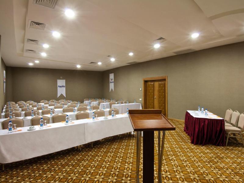 A conference room with rows of seated tables and a lectern at the front.