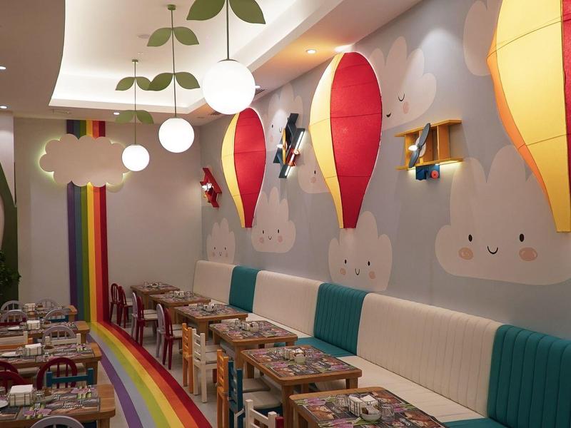Colorful kids' area with rainbow decor, cozy seating, and hot air balloon-shaped lights.