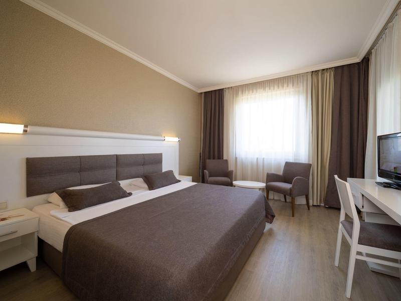 Modern hotel room with double bed, desk, TV, and two chairs by the window.