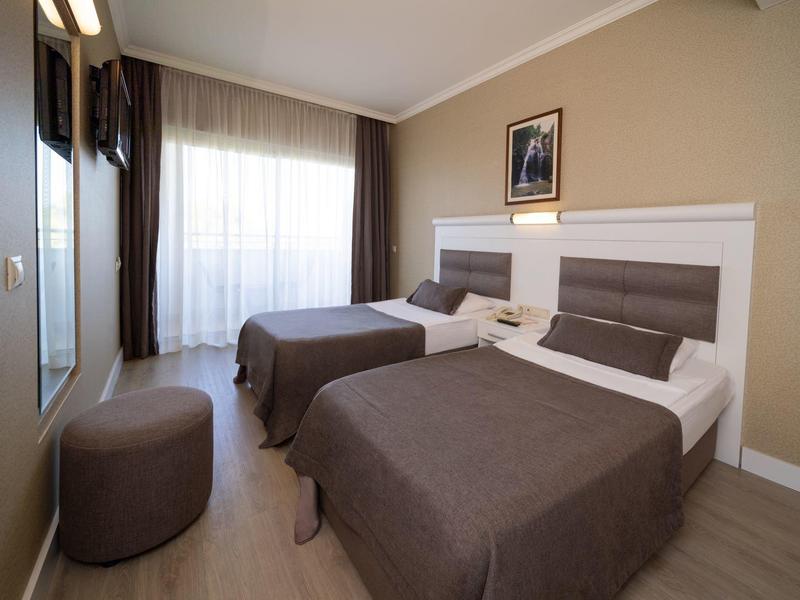 Hotel room with two single beds, brown bedspreads, and large window with curtains.