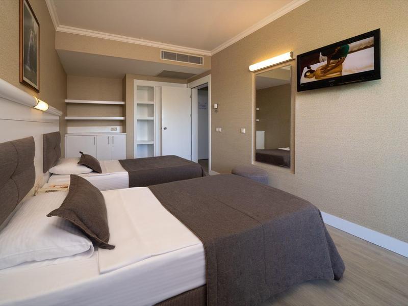 Modern hotel room with two beds, gray bedding, and minimalist decor.