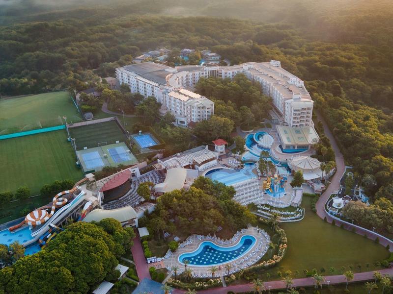 Aerial view of a resort with multiple pools and surrounding forest area at sunset.