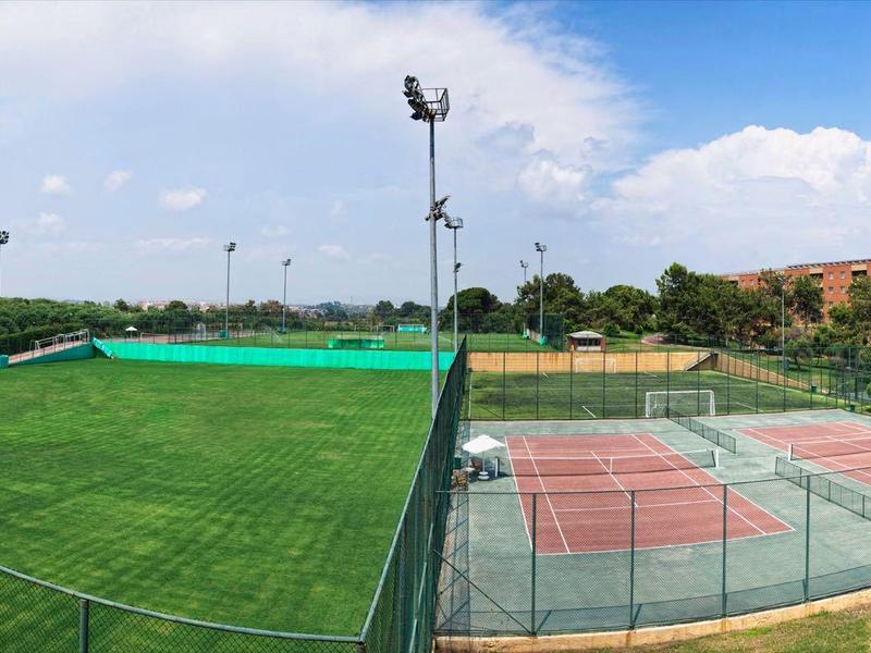 Panoramic view of an outdoor sports complex with tennis and soccer fields near hotel buildings.