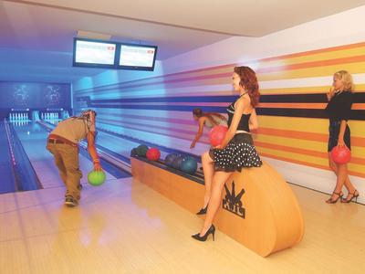 Zwei Frauen und zwei Männer beim Bowling in einer farbig gestreiften Bowlingbahn.