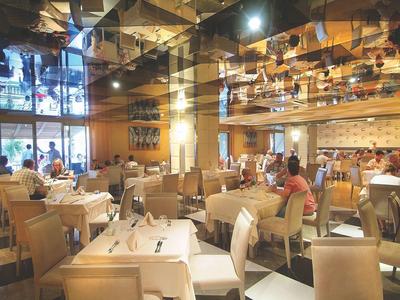 Restaurant élégant avec tables blanches, chaises beiges et grands miroirs au plafond.