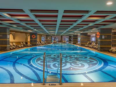 Piscine intérieure de luxe avec sol décoré, chaises longues et éclairage chaleureux.