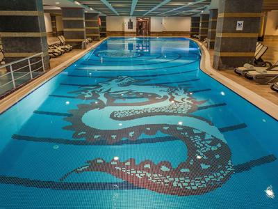 Piscine intérieure avec un grand dragon décoratif au fond, entourée de chaises longues.