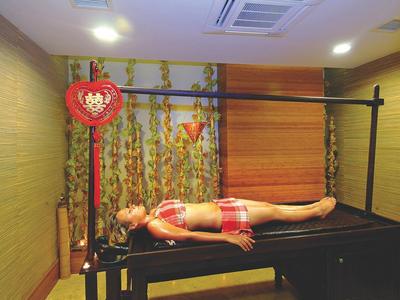Femme allongée sur une table de massage dans une pièce décorée avec un motif floral et une lanterne rouge.