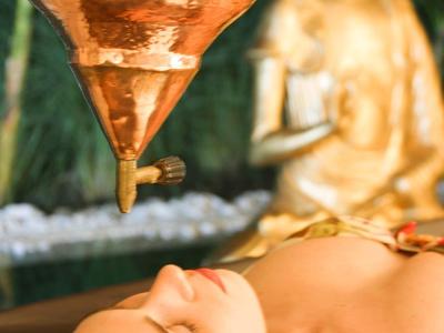 Femme se relaxant sous une fontaine en cuivre dans un spa.