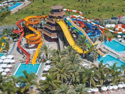 Waterpark met meerdere kleurrijke glijbanen, zwembaden en palmbomen in een resort.