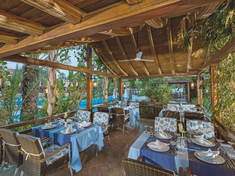 Restaurant en terrasse avec décoration en bois, tables dressées et vue sur la végétation et la mer.