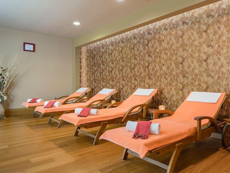 Quatre chaises longues orange alignées près d'un mur décoré, dans une salle lumineuse.