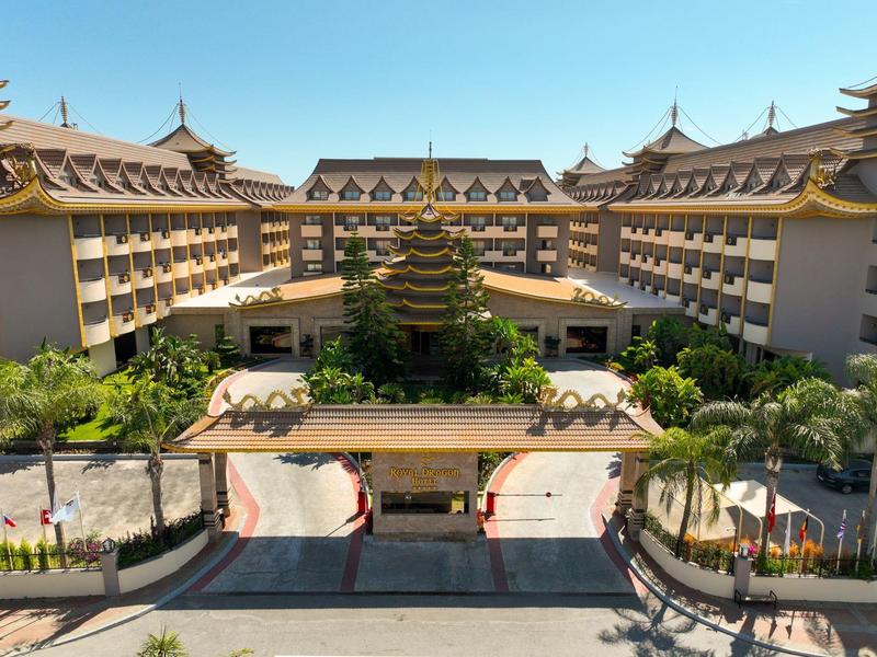 Vue d'un hôtel avec une entrée principale et des jardins tropicaux sous un ciel clair.