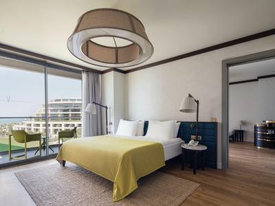 Habitación de hotel moderna con cama doble, manta amarilla y balcón con vista al mar.