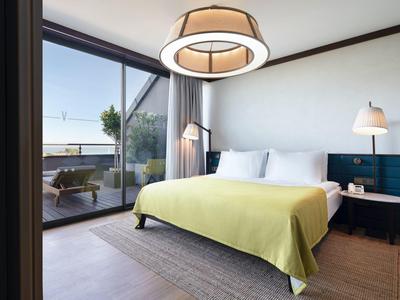 Dormitorio luminoso con cama grande, manta amarilla y vista a terraza con vistas al mar.