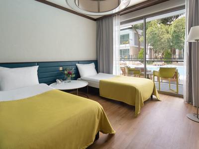 Habitación de hotel moderna con dos camas, mantas amarillas y gran ventana con vista a la terraza.