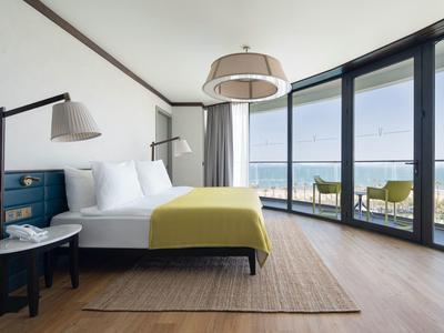 Habitación de hotel moderna con cama grande y balcón con vista al mar.