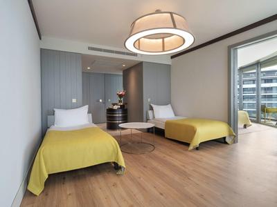 Habitación de hotel luminosa con dos camas individuales, suelo de madera y balcón con vista a edificios vecinos.