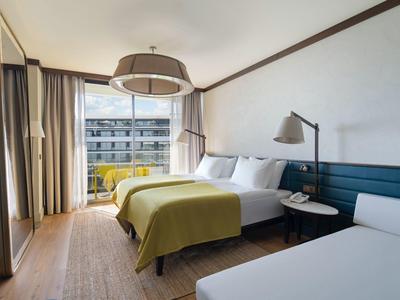 Habitación de hotel moderna con cama doble, sofá cama y balcón con vistas urbanas.