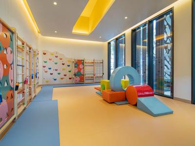 Sala de juegos colorida y moderna con muro de escalada, colchonetas y grandes ventanas en el hotel.