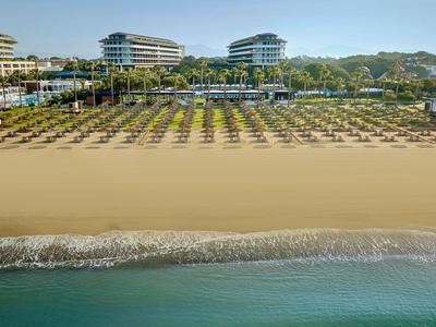 Ampia spiaggia sabbiosa con lettini e ombrelloni davanti a moderni edifici di hotel in una giornata di sole.