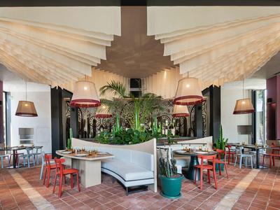Restaurante moderno de hotel con plantas centrales, sillas de colores y lámparas colgantes.