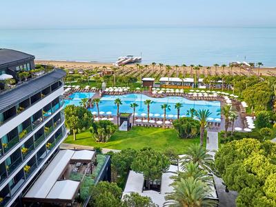 Moderner Hotelkomplex mit Pool, Sonnenschirmen und Blick auf das Meer und einen Sandstrand.