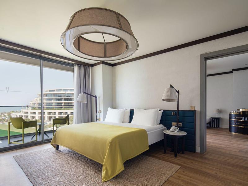 Habitación de hotel moderna con cama doble, manta amarilla y balcón con vista al mar.