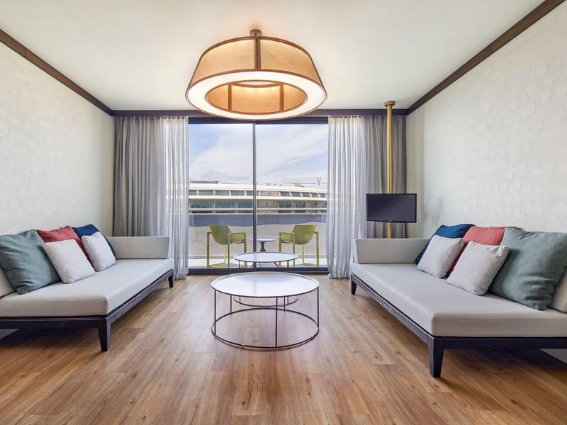 Sala moderna con grandes ventanas, dos sofás, alfombra y vista al agua y edificios.