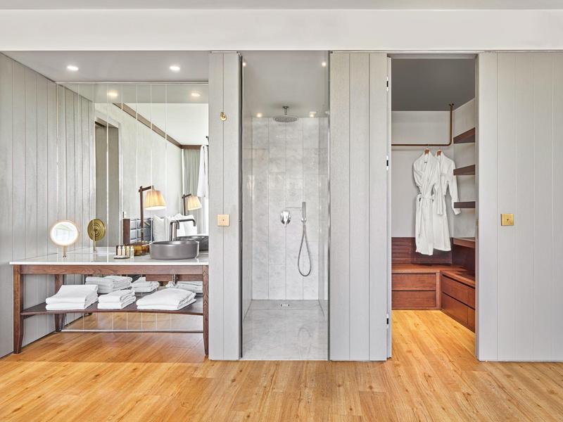 Baño moderno con ducha a ras de suelo, estantes de madera y un gran espejo sobre el lavabo.