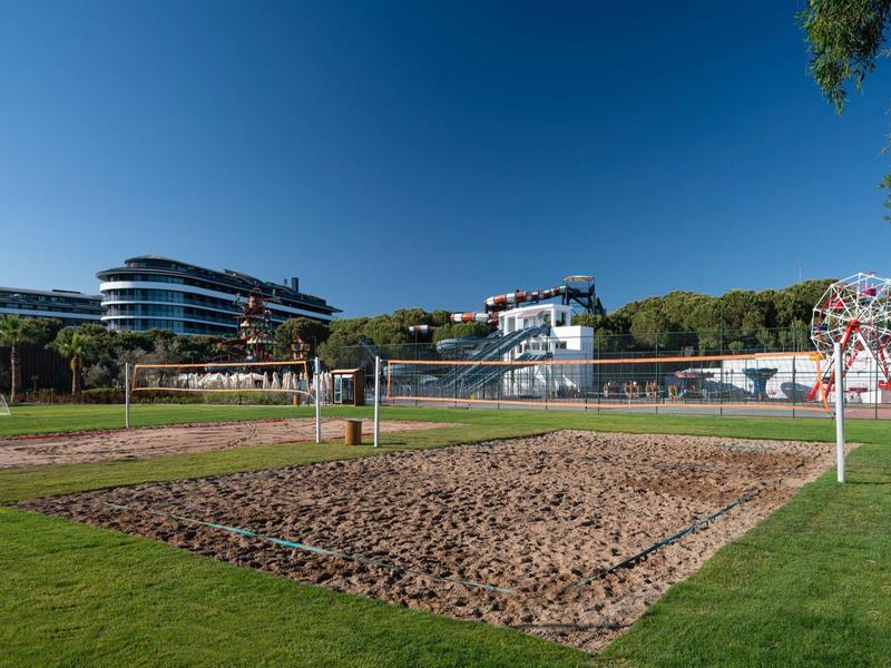 Campo de voleibol de arena en césped verde junto a hoteles modernos bajo un cielo despejado.