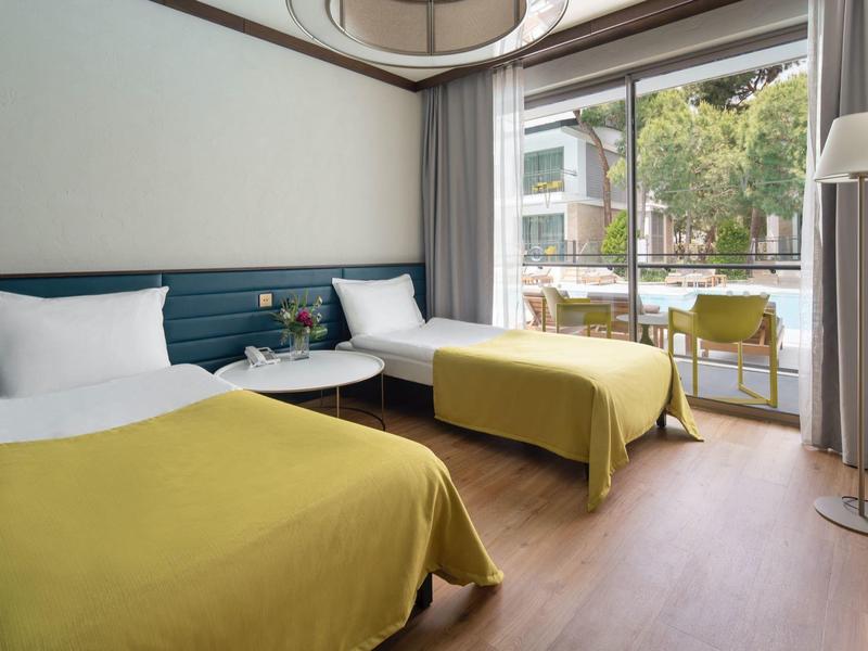 Habitación de hotel moderna con dos camas, mantas amarillas y gran ventana con vista a la terraza.