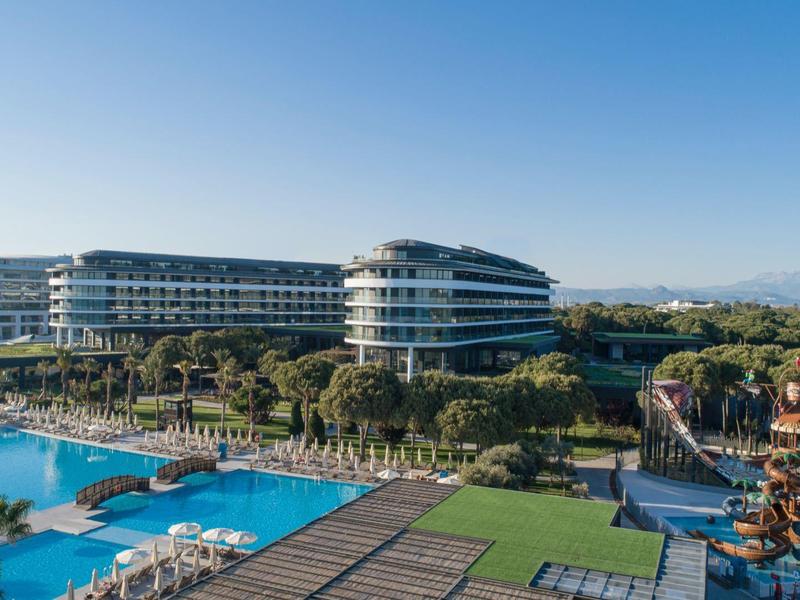 Gran resort con edificios modernos, piscinas, sombrillas y áreas verdes bajo un cielo claro.
