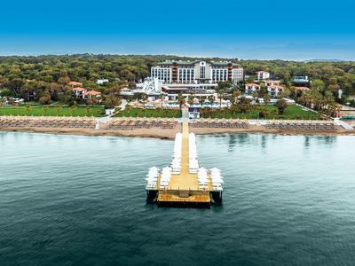 Langes Pier mit Pavillons führt zu großem Hotel in grünem Küstenbereich unter blauem Himmel.
