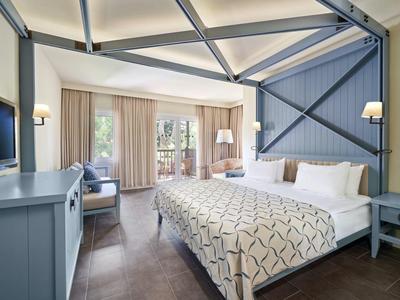 Helles Schlafzimmer mit großem Bett, blau-grauen Holzakzenten und Fenster mit Vorhängen.