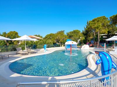 Kleiner Rundpool mit Wasserspiel, Sonnenschirmen und Liegestühlen im Garten bei blauem Himmel.