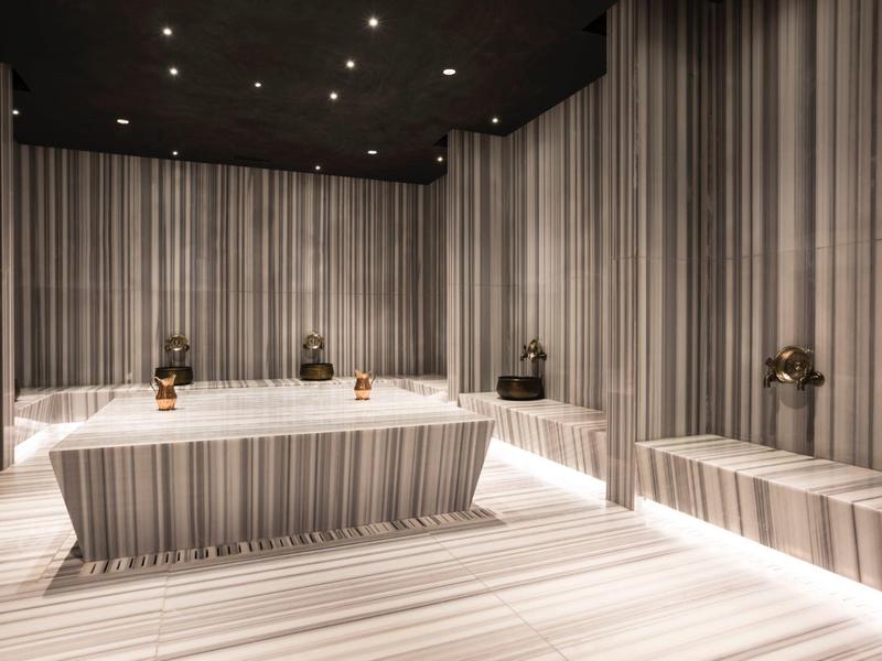 Luxusní spa místnost s páskovanými mramorovými lavicemi a měkkým teplým osvětlením.