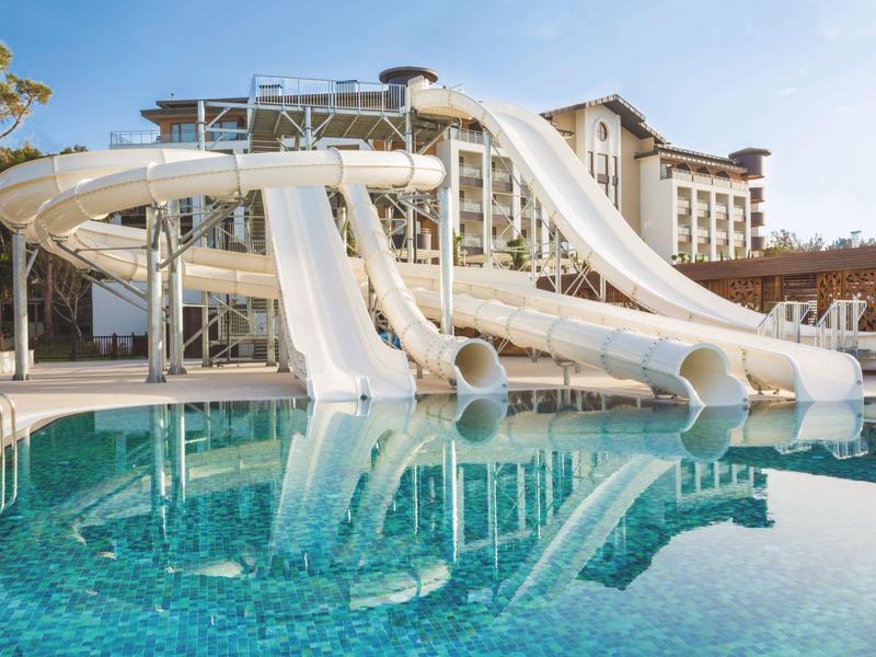 Velké vodní skluzavky vedoucí do čirého modrého bazénu v resortu pod slunečnou oblohou.