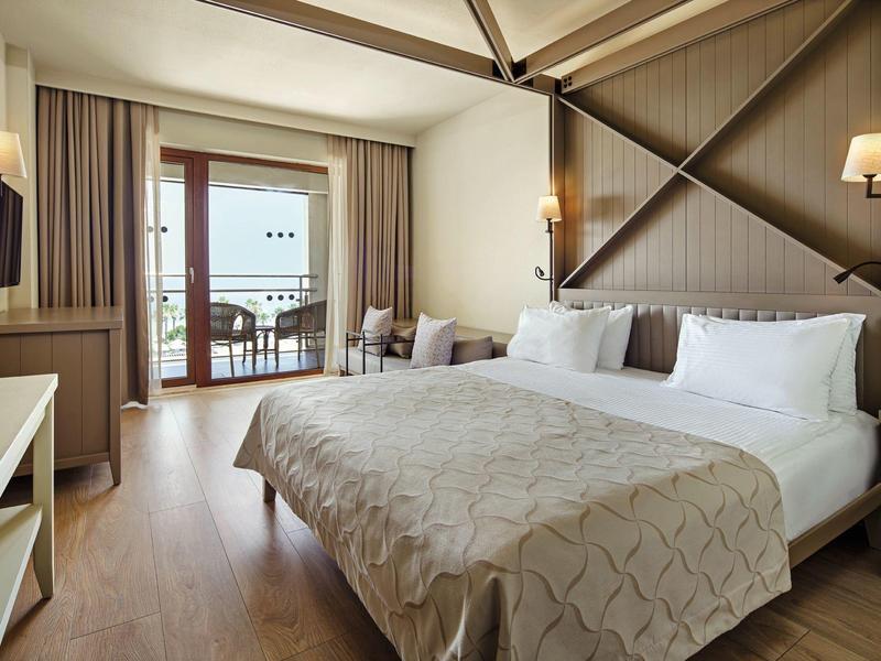 Prostorný hotelový pokoj s velkou postelí, balkonem a pohodlným posezením s teplým osvětlením.