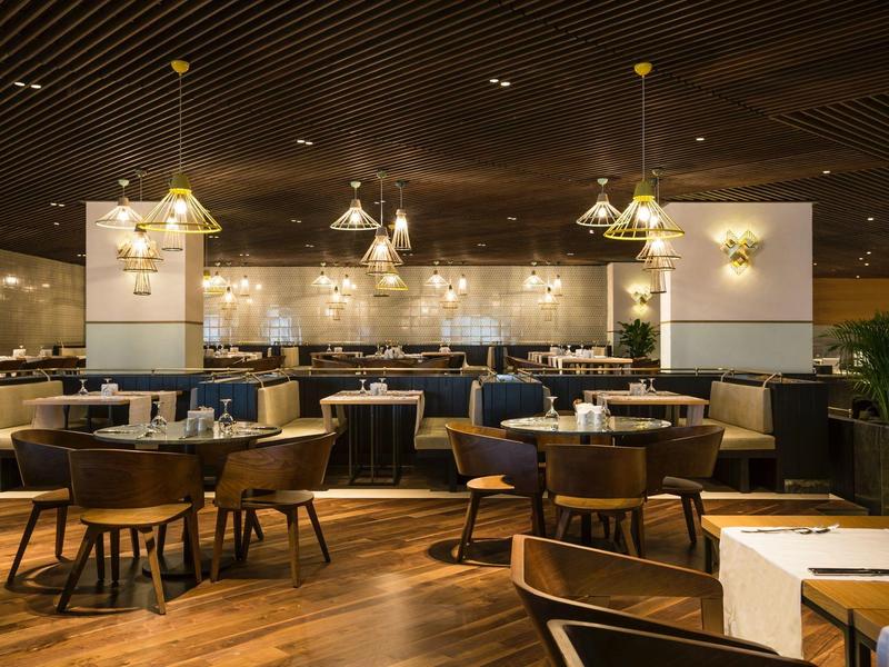 Moderní restaurace s dřevěnou podlahou, osvětlením na sloupech a elegantními závěsnými lampami.