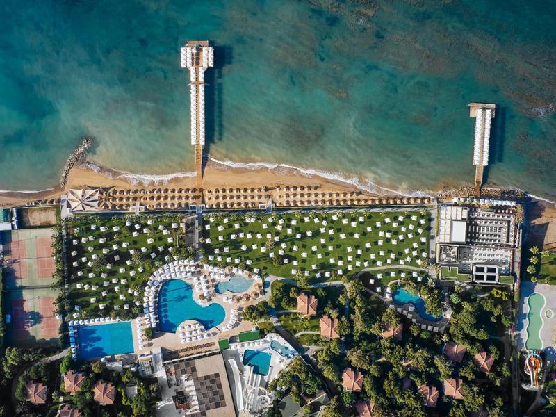 Letecký pohled na plážové letovisko se dvěma moly, bazény a zeleným trávníkem s deštníky.