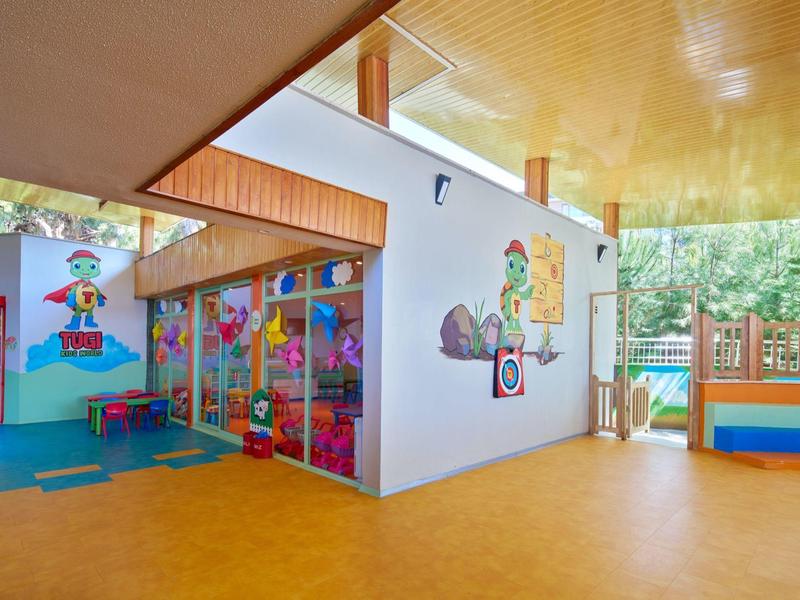 Světlá vnitřní herna s barevnou nástěnnou malbou a velkými okny s výhledem na zeleň.