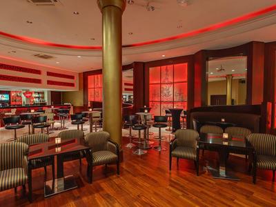 Zona elegante de restaurante de hotel con suelo de madera, sillones cómodos y luz roja en el techo.