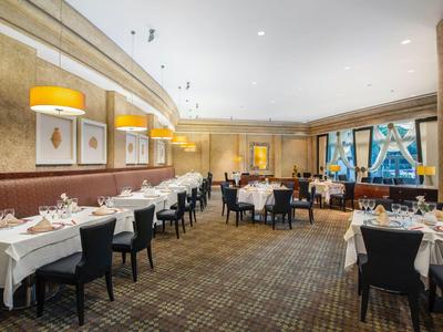 Elegantní hotelová restaurace s prostřenými stoly, žlutými nástěnnými lampami a kobercem.