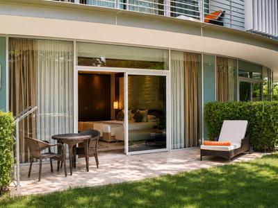 Giardino d'hotel moderno con terrazza, mobili da esterno e sdraio davanti a grandi finestre in vetro.