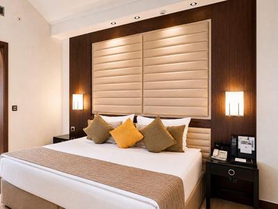 Camera d'hotel moderna con letto grande, testiera in legno e cuscini decorativi.