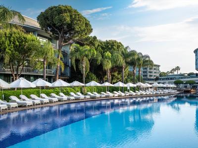 Hotelpool mit Liegestühlen, Sonnenschirmen und Palmen bei klarem Himmel.